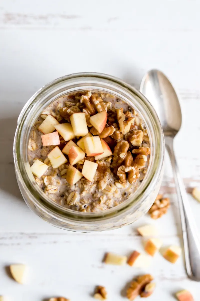 Overhead shot of apple cinnamon overnight oats in glass jar with diced apples walnuts and spoon.